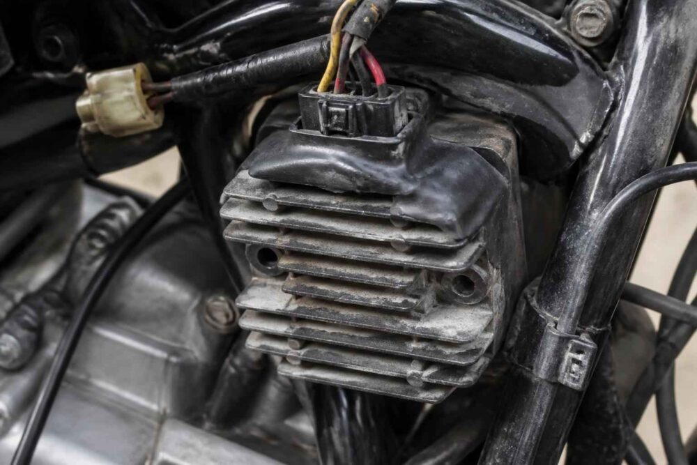 Zużyty regulator napięcia z przewodami zamontowany przy silniku motocykla